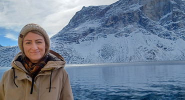 Eine Frau steht vor einer Winterlandschaft mit Meer und Bergen