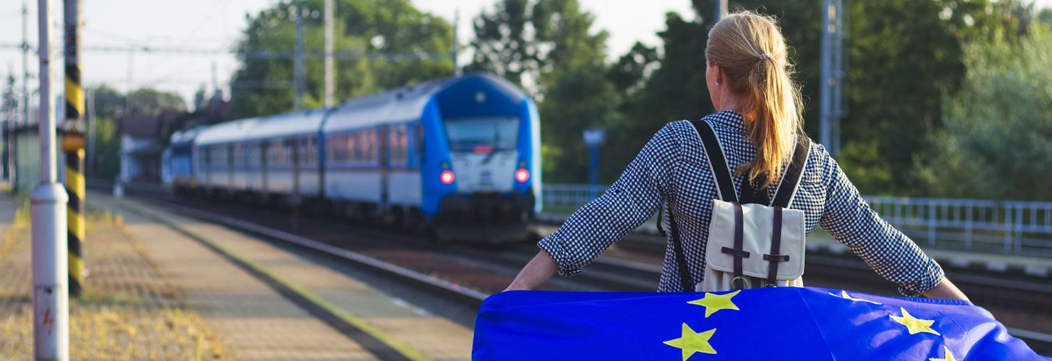 Junge Frau mit EU-Flagge am Bahnhof
